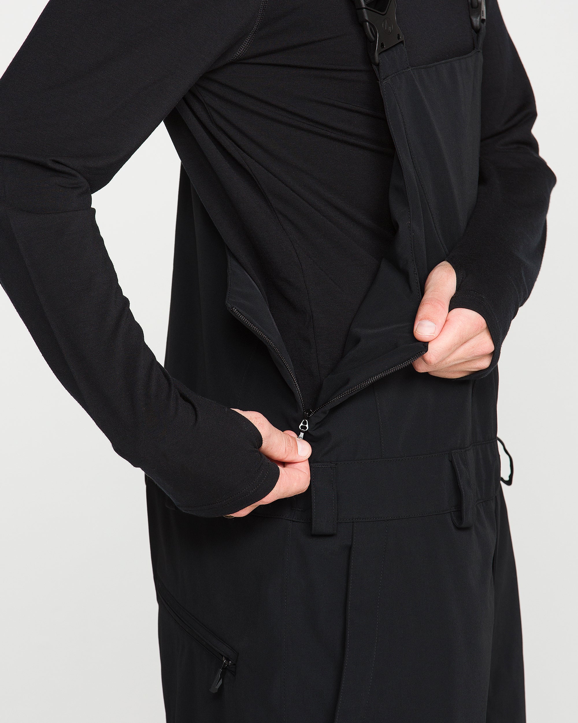 Black bib overall front view with zip pocket, adjustable waist tie, and cargo pockets