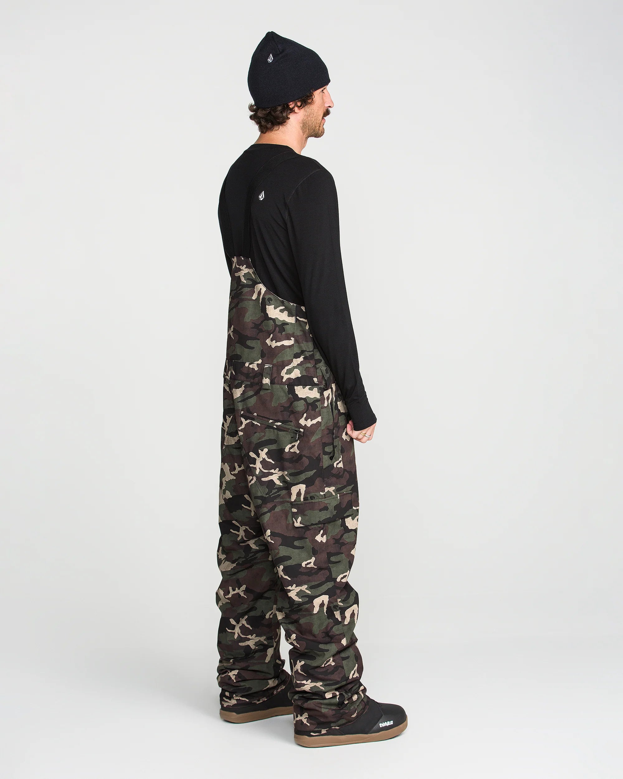 Camouflage bib overalls worn from side with black straps over the chest