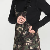 Camo bib overalls front view with black overlay straps and small chest label
