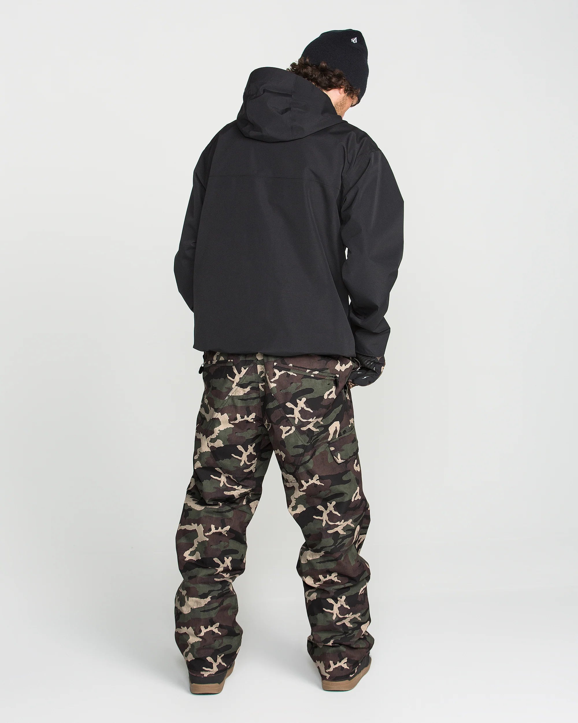 Camouflage bib overalls shown from back with black hooded jacket and boots