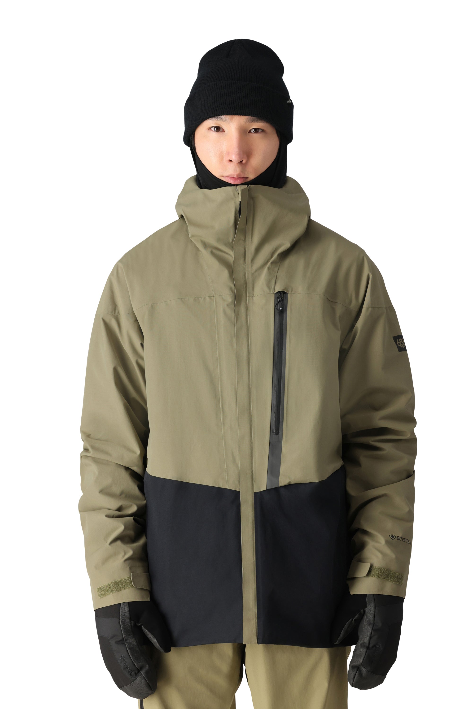 The 686 Gore-Tex shell jacket in this front view image has a khaki upper body and black lower section, with no visible logos.
