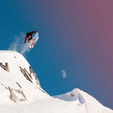 A skier wearing a red jacket is seen skiing downhill on a mountain. The skis are Salomon S/Lab QST Blank Skis 2026, and the person is in mid-air while performing a jump.