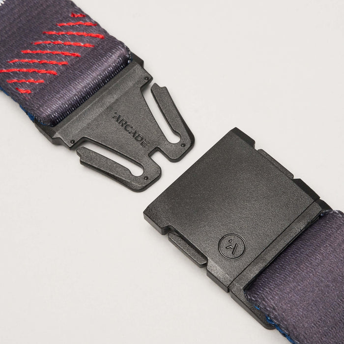 Close-up of a black plastic buckle with the brand name "Arcade" on the clasp, attached to a charcoal gray belt with red and blue embroidered designs.