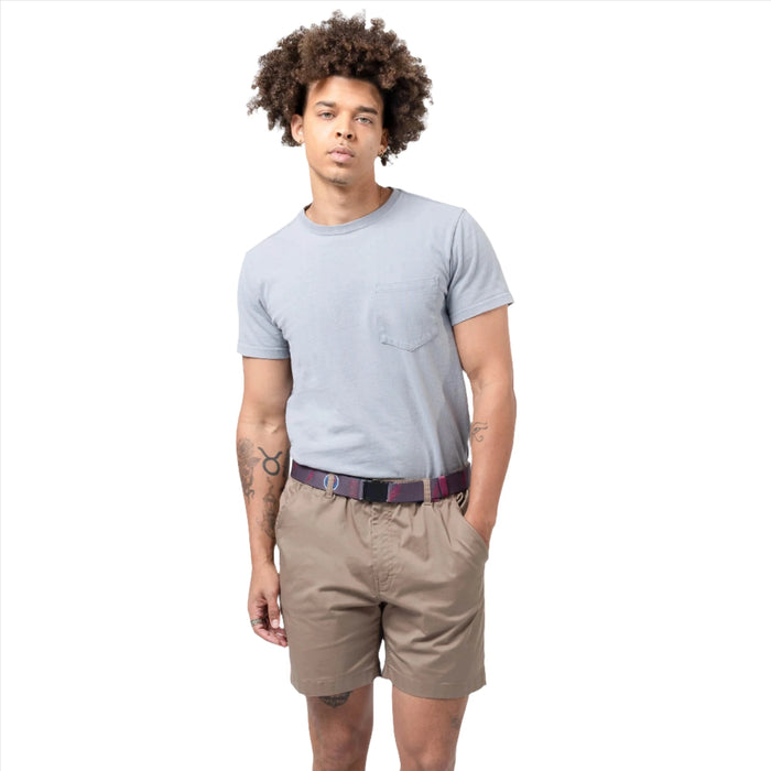 A man with curly hair wearing a light gray t-shirt and khaki shorts, showcasing a charcoal gray belt with red and blue embroidered designs.