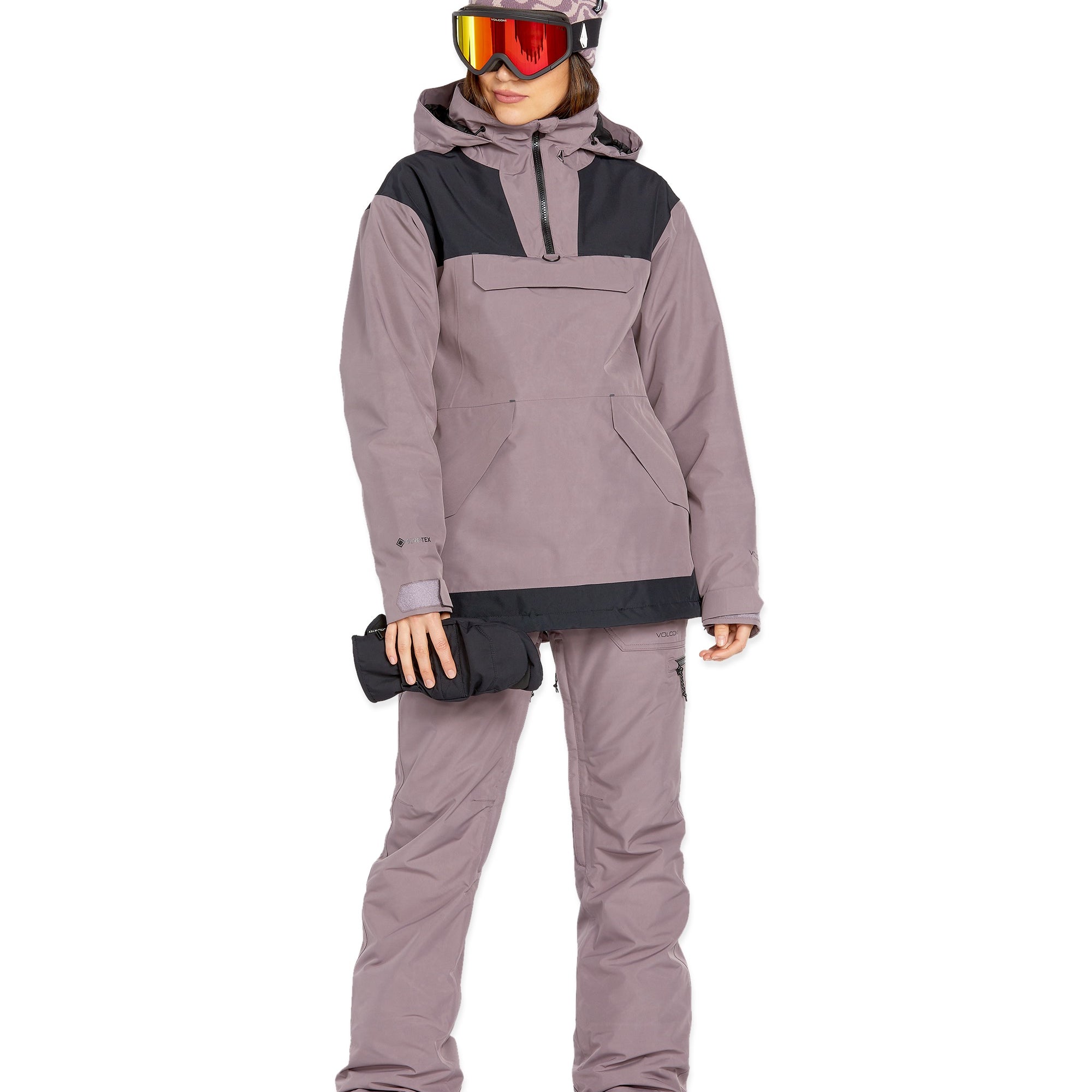 Volcom Women's Fern Insulated GORE-TEX Pullover - A woman wearing a mauve and black insulated pullover with a hood, holding a black glove in her right hand.