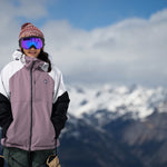 Volcom Women's Agate Ins Jacket 2025 - A woman wearing a white, mauve and black jacket with a hood, standing in front of snowy mountains.