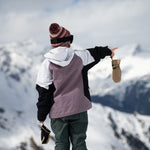 Volcom Women's Agate Ins Jacket 2025 - A woman wearing a white, black, and purple jacket with a hood, holding a pair of gloves in her left hand while pointing to the right.