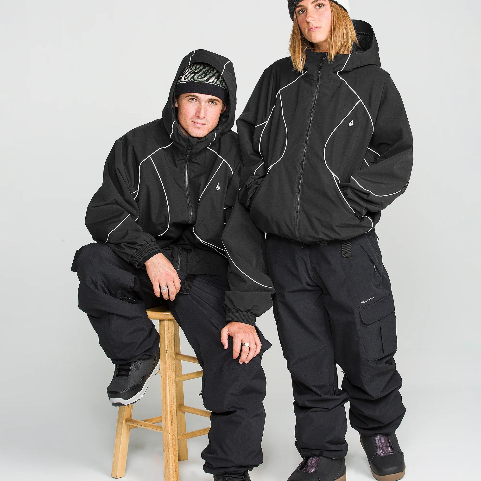 Women's black ski jacket with hood, white piping, zip front, and cargo-style pockets.