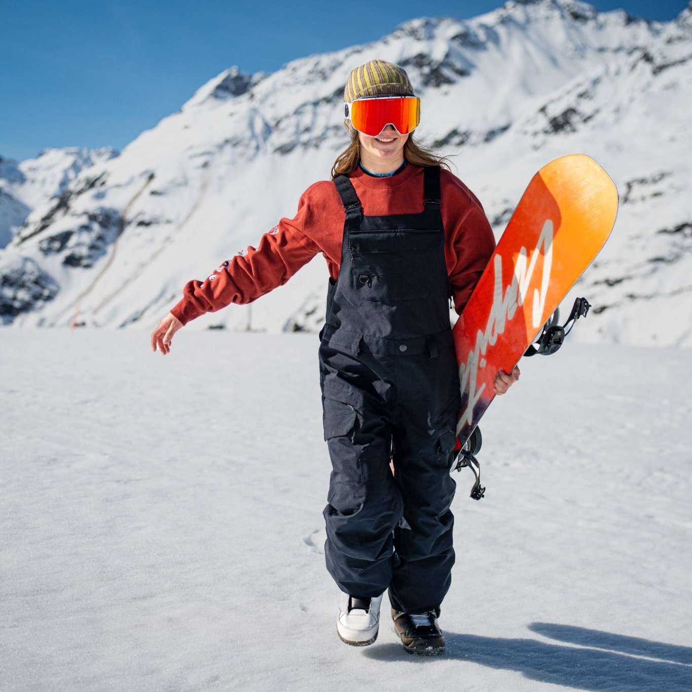 Volcom Women's Creston 3D Stretch Bib Overall - Black bib overalls with white logo on left thigh and right chest, worn by a woman standing in snowy terrain.