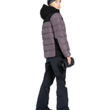 Volcom Women's Elm Stretch GORE-TEX Bib Overall - A woman wearing a black and white striped beanie, a gray puffer jacket with a black hood, and black snow pants with a zippered pocket on the thigh.