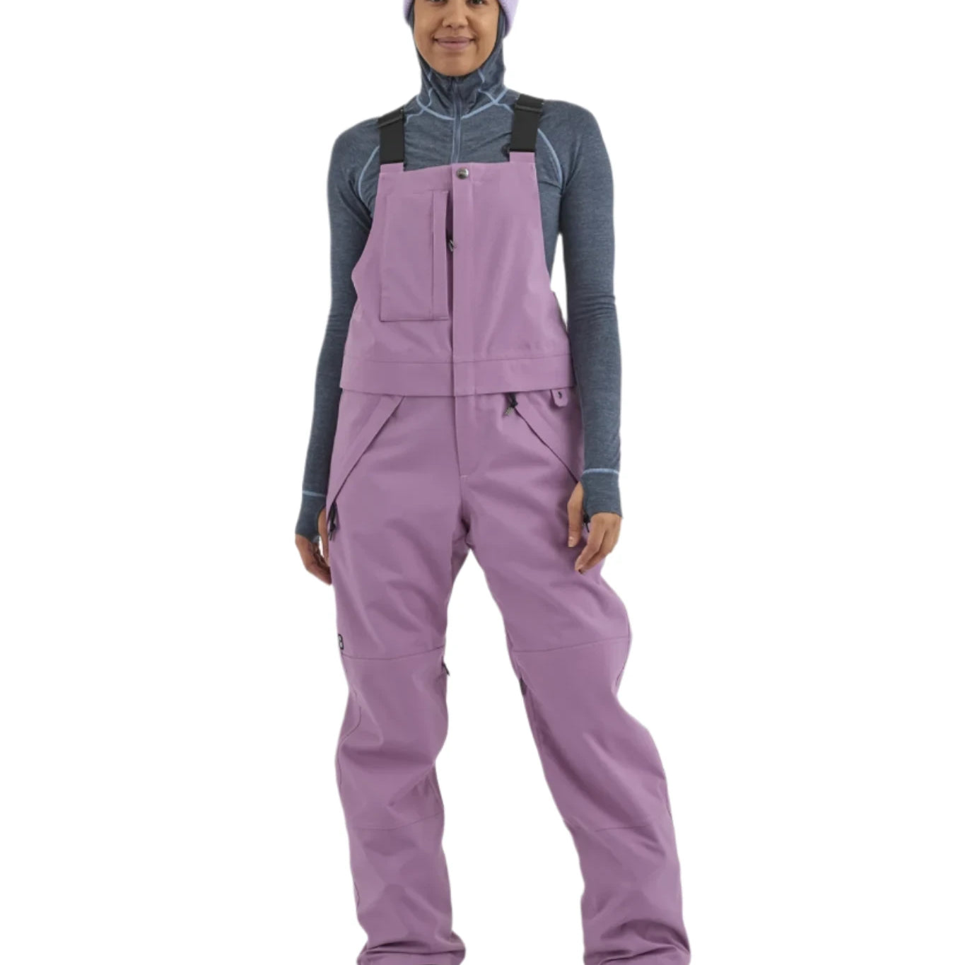 Airblaster Women's Hot Bib Shell 2025 - A woman wearing a grey-blue shell with white stitching and a high collar, paired with black pants and boots.