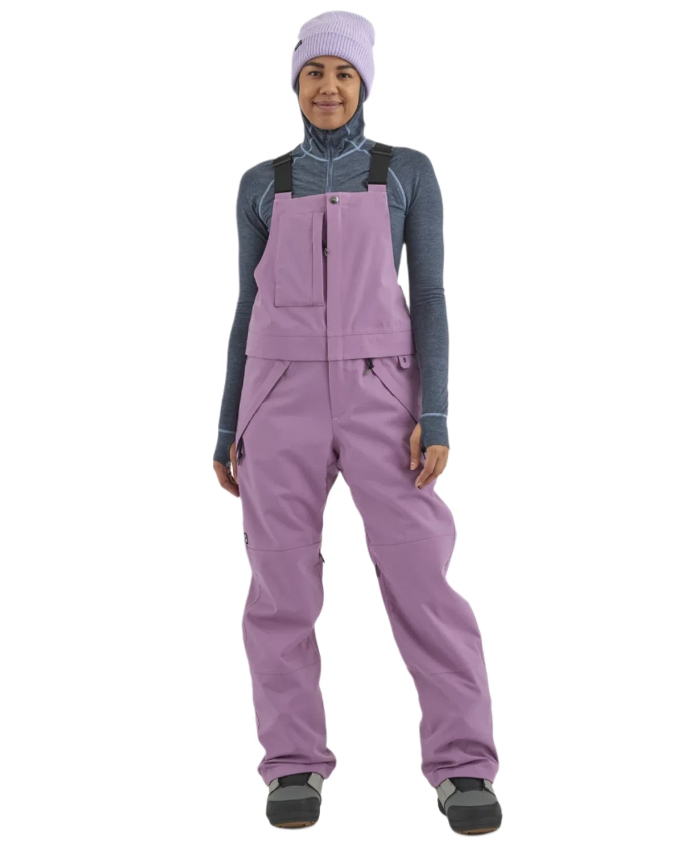 Airblaster Women's Hot Bib Shell 2025 - A woman wearing a grey-blue shell with white stitching and a high collar, paired with black pants and boots.