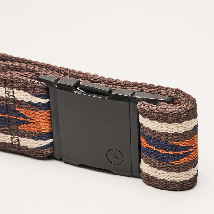 Close-up of a belt with a black buckle, showing the end of the belt looped through the buckle. The belt features a geometric pattern in brown, blue, white, and orange stripes.