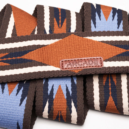 Close-up of a belt with a geometric pattern in brown, blue, and white. The belt features zigzag and diamond shapes, with a small rectangular tag that says 'Arcade' in the center.