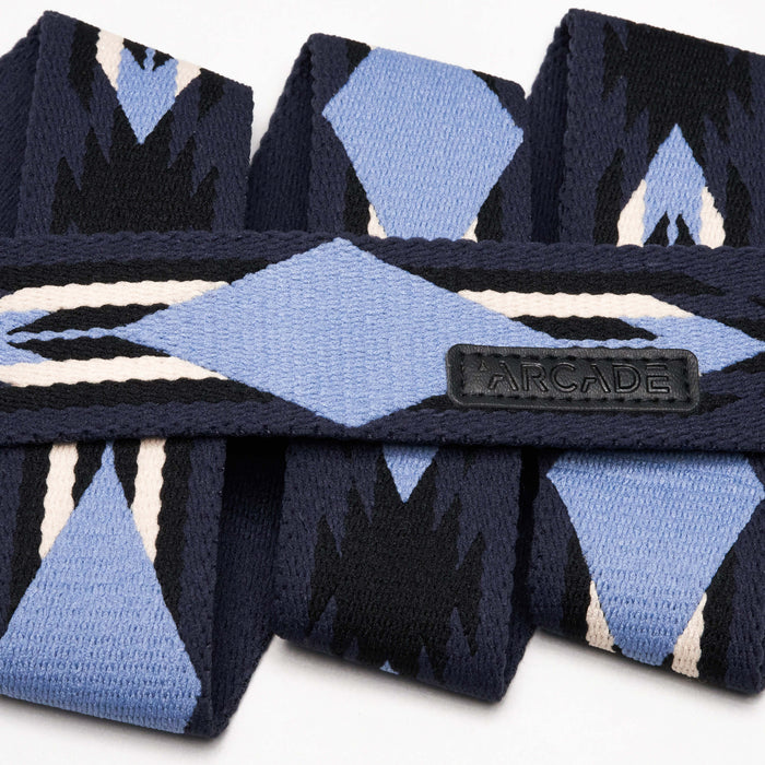 Close-up view of a navy blue belt with a geometric pattern in light blue, black, and white, showing a leather tag with the word 'Arcade' stitched on it.