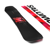 Salomon Women's No Drama Snowboard 2026 - A black snowboard with a red and white logo featuring a woman in a bikini top and shorts, set against a light gray background.