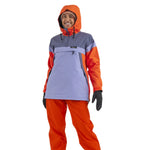Airblaster Women's Trenchover Insulated Jacket 2025 - A woman wearing a grey and orange jacket with an orange hood, standing against a white background.