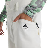 Burton Women's Marcy 2L High Rise Stretch Pants 2025 - A pair of white snow pants with a black logo on the left thigh and a zippered pocket on the right side.