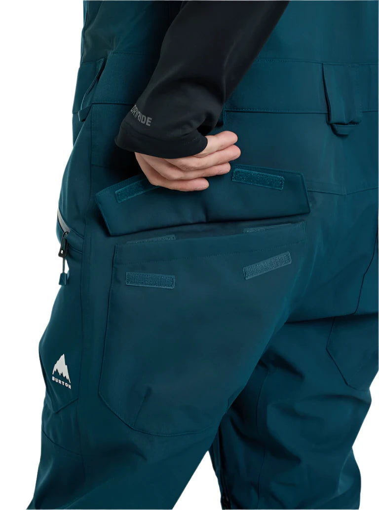 Burton Reserve Bib Pant 2025 - Dark-colored bib pant with a white logo on the left leg featuring a mountain peak design and the word "BURTON" in small letters underneath.