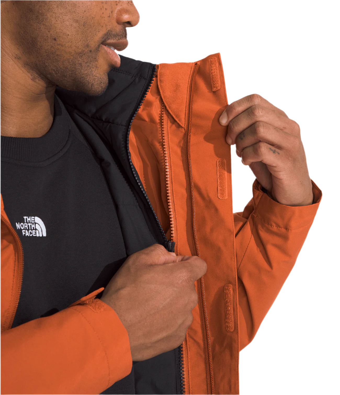 North Face Carto Triclimate Jacket - A man wearing a black and burnt orange jacket with a white logo on the left chest area, zipping up the front of the jacket.