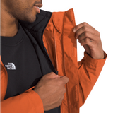North Face Carto Triclimate Jacket - A man wearing a black and burnt orange jacket with a white logo on the left chest area, zipping up the front of the jacket.