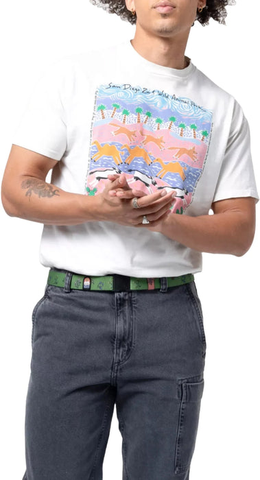 A person wearing a white t-shirt with a colorful graphic design and dark blue jeans. The person is wearing a green belt with a floral pattern and a small embroidered patch visible near the buckle.