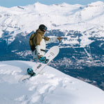 Nidecker Alpha Snowboard 2025 - A white snowboard with black and blue bindings, featuring a wolf logo on its bottom edge.