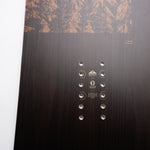 Nidecker Escape Plus Snowboard 2025 - A dark brown snowboard with a wood grain texture and a mountain range design at the top.