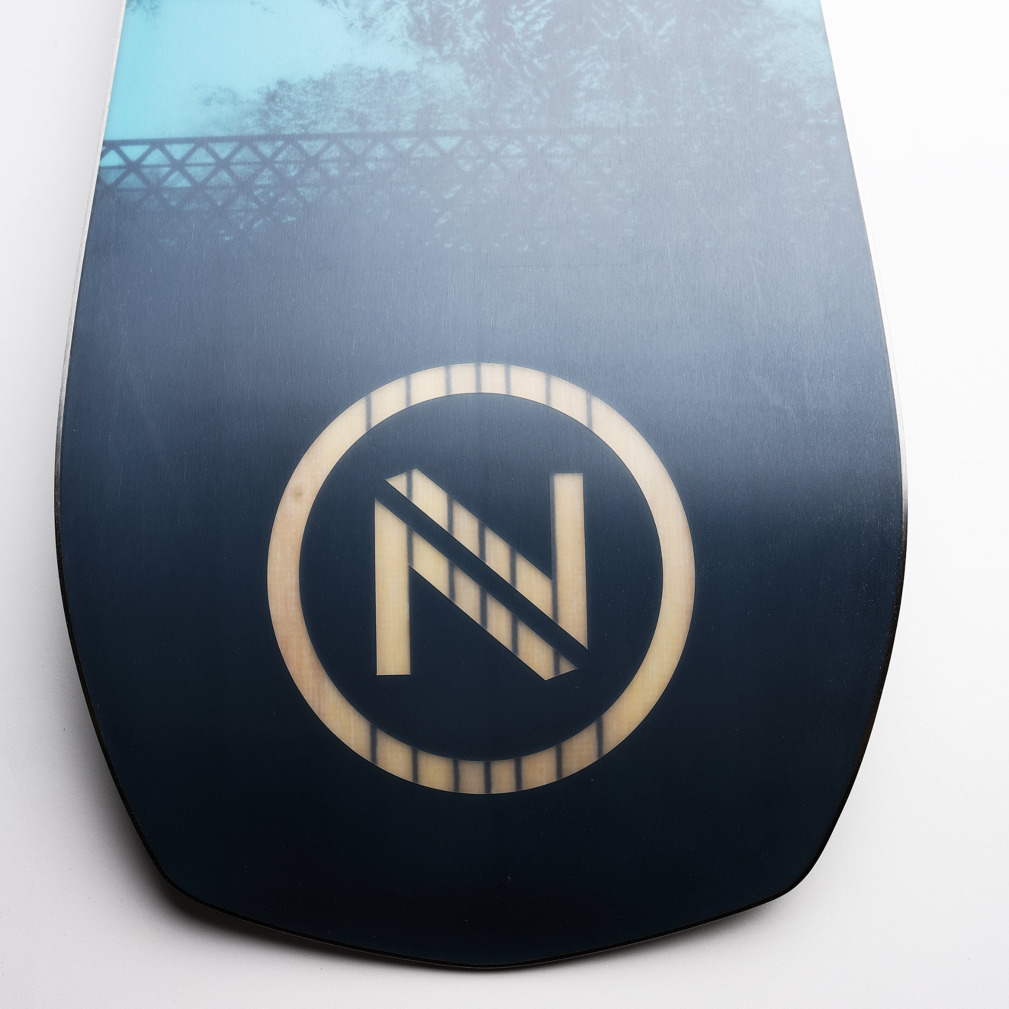 Nidecker Escape Plus Snowboard 2025 - A black snowboard with a white logo featuring an "N" and diagonal line, set against a light blue background.