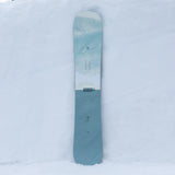 Nidecker Escape Snowboard 2025 - A light blue snowboard with a white stripe and forest green trees printed on it.