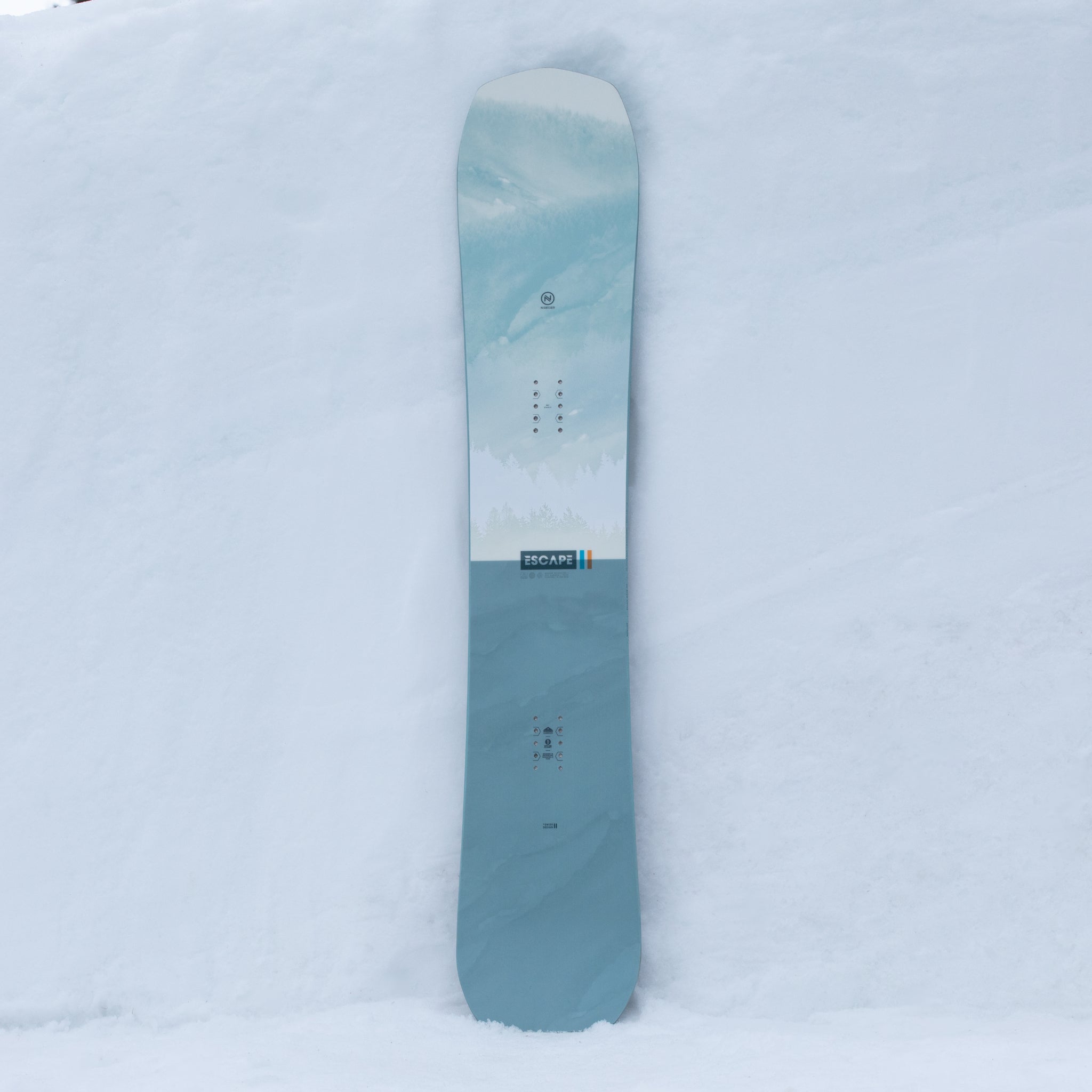 Nidecker Escape Snowboard 2025 - A light blue snowboard with a white stripe and forest green trees printed on it.