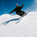 Nidecker Merc Snowboard 2025 - A white snowboard with a black logo on its bottom edge, being ridden by a man in mid-air.