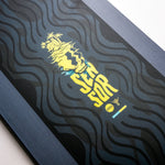 Nidecker Sensor Youth Snowboard 2025 - A navy blue snowboard with a white and yellow graphic of a skull wearing goggles, riding down a mountain.
