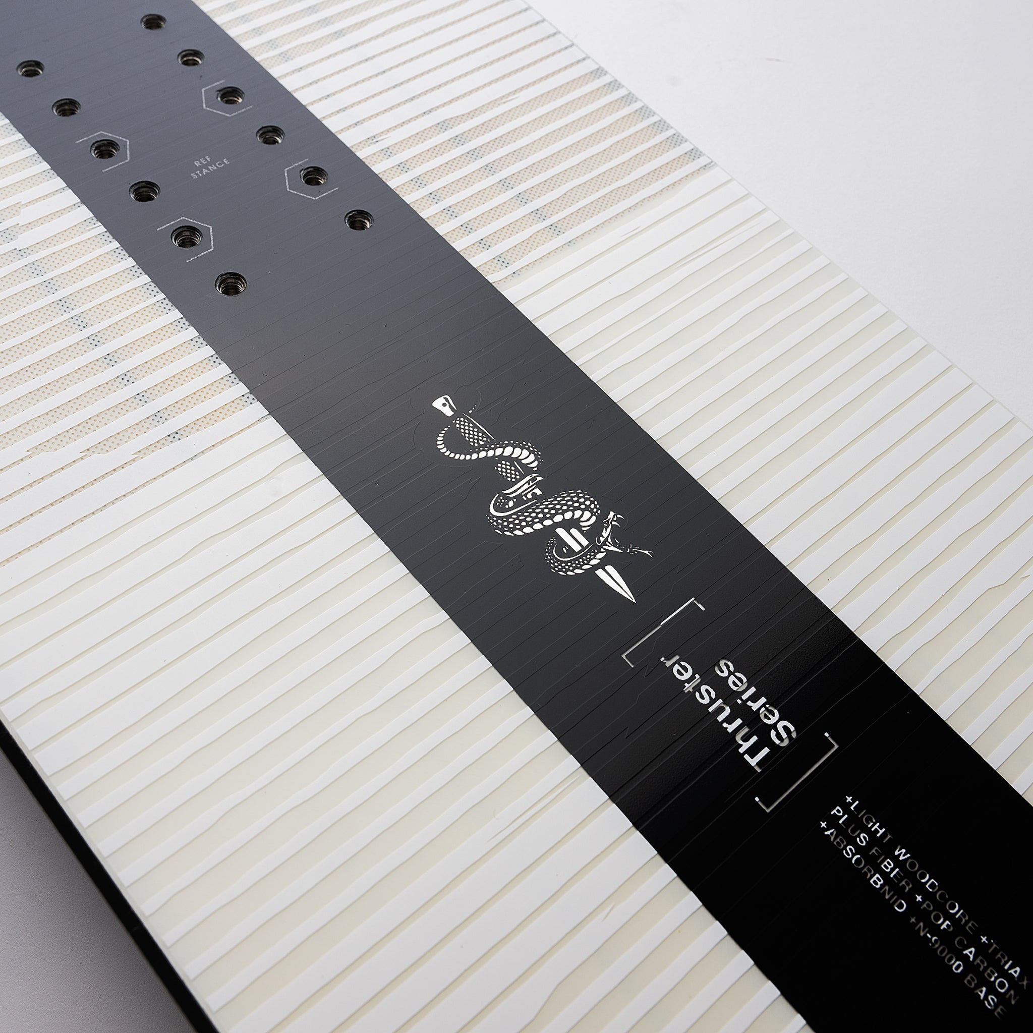 Nidecker Thruster Snowboard 2025 - A black snowboard with a white snake logo and white lettering on top of a light-colored wood grain background.