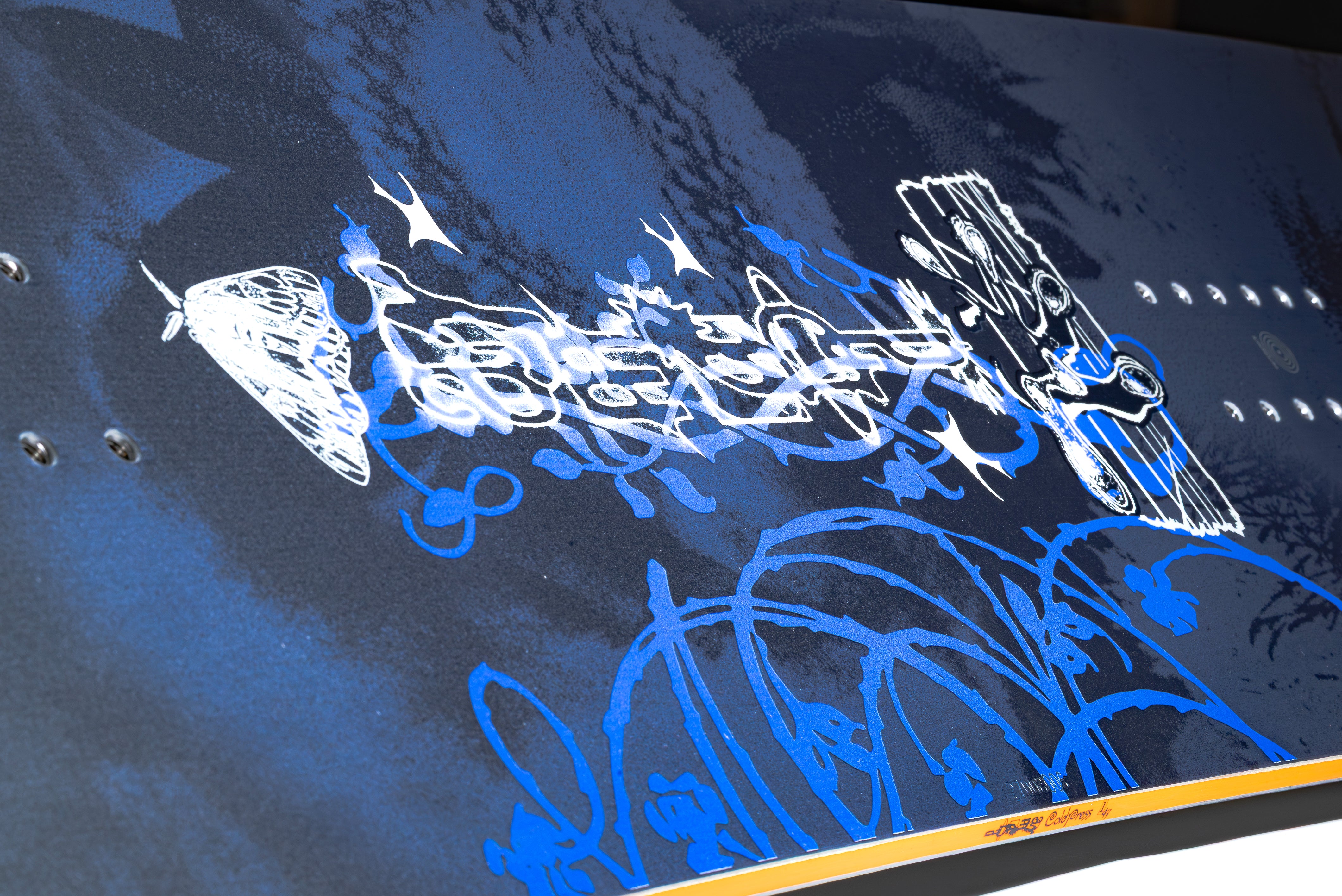 Close-up of dark blue snowboard with white script graphics and blue artwork