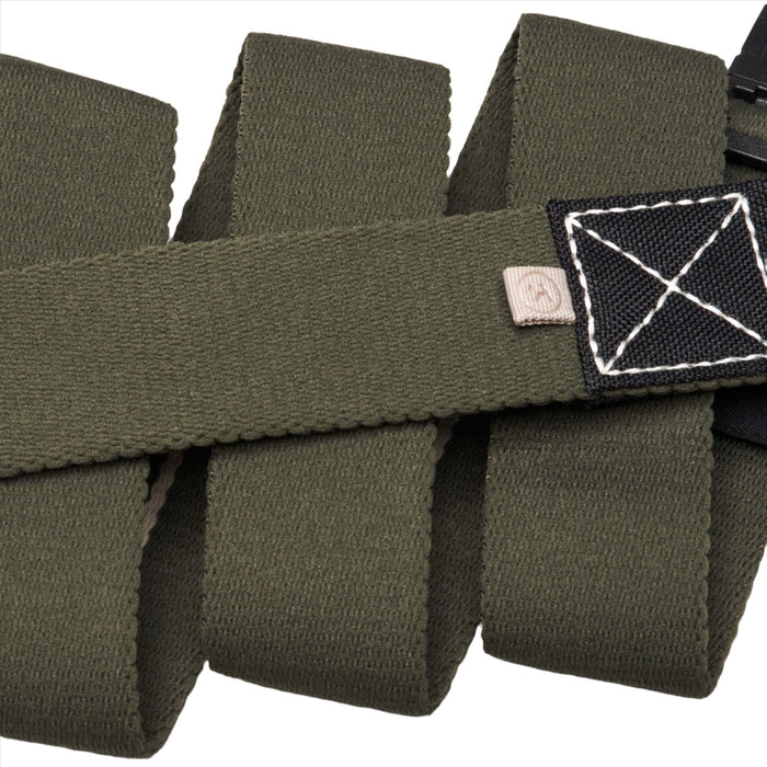 A close-up of an ivy green fabric belt with a black rectangular patch featuring white stitched detailing. The belt is folded multiple times, highlighting its texture and the small logo tag next to the patch.