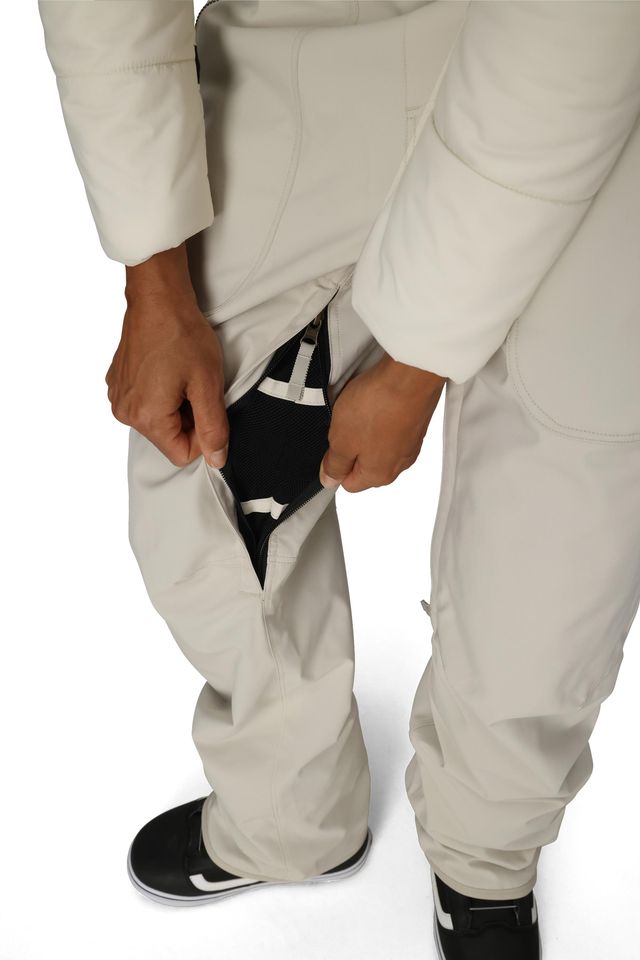 Close-up of off-white insulated bib overalls with black inner gaiter and side zipper opening.