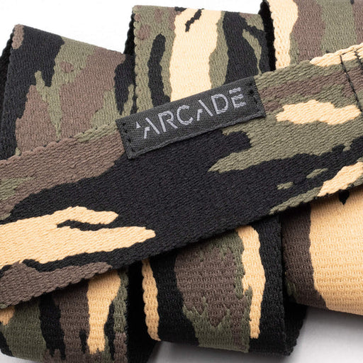 Close-up view of a camouflage-patterned belt in shades of green, brown, and beige, showing a fabric tag with the word 'Arcade' stitched on it.