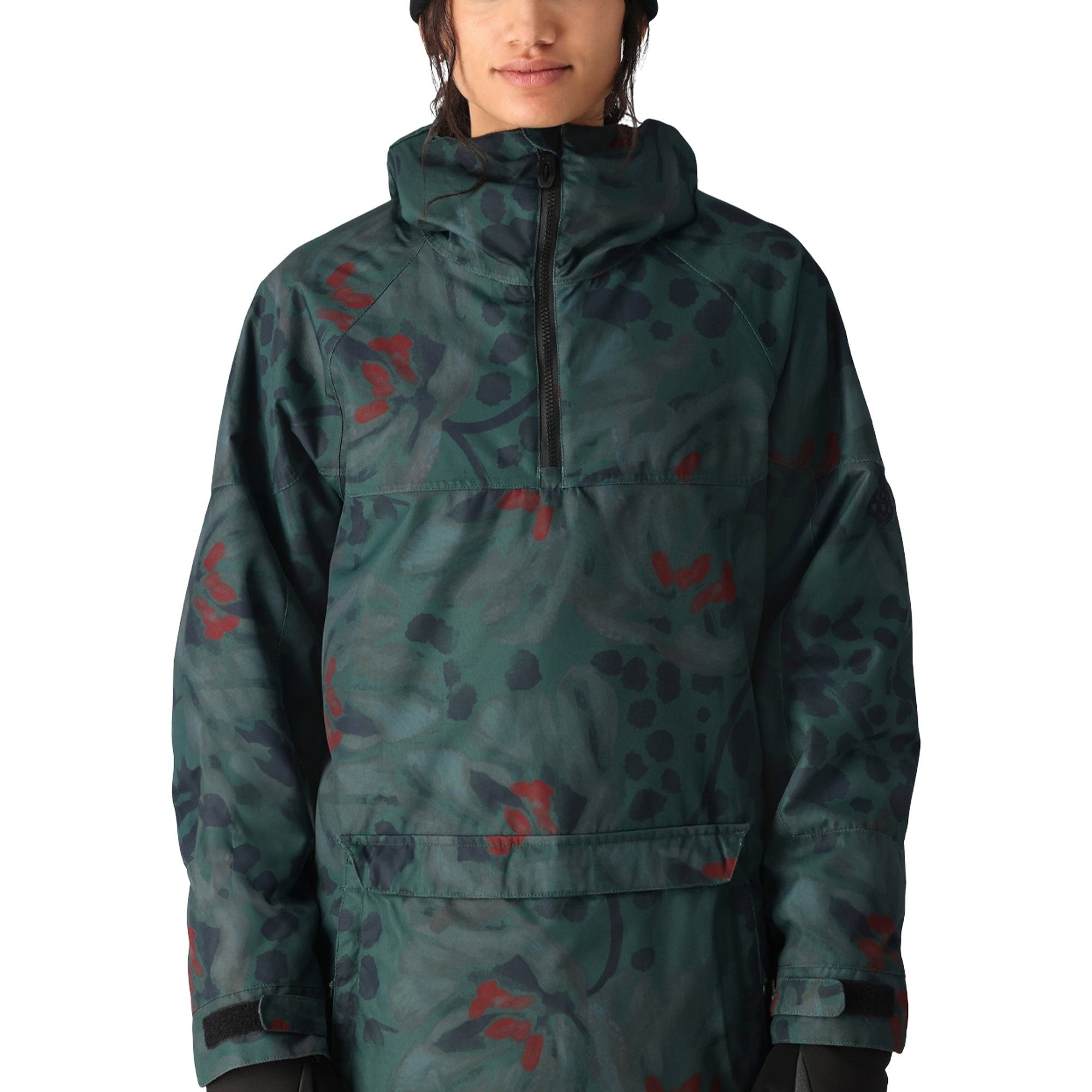 The 686 Women's Upton Insulated Anorak Jacket features a green camouflage pattern with red accents and a black zipper on the front.