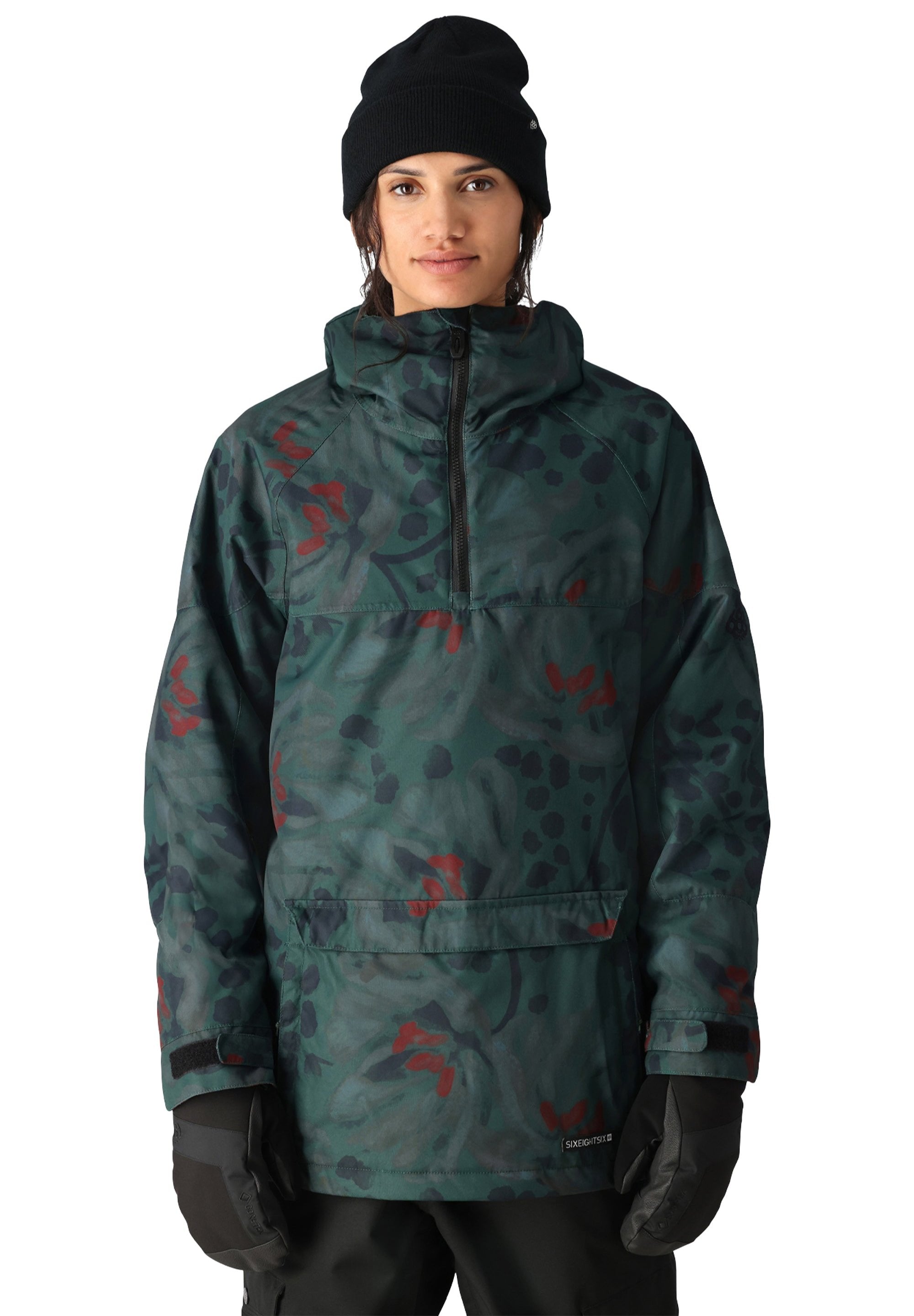 The 686 Women's Upton Insulated Anorak Jacket features a green camouflage pattern with red accents and a black zipper on the front.