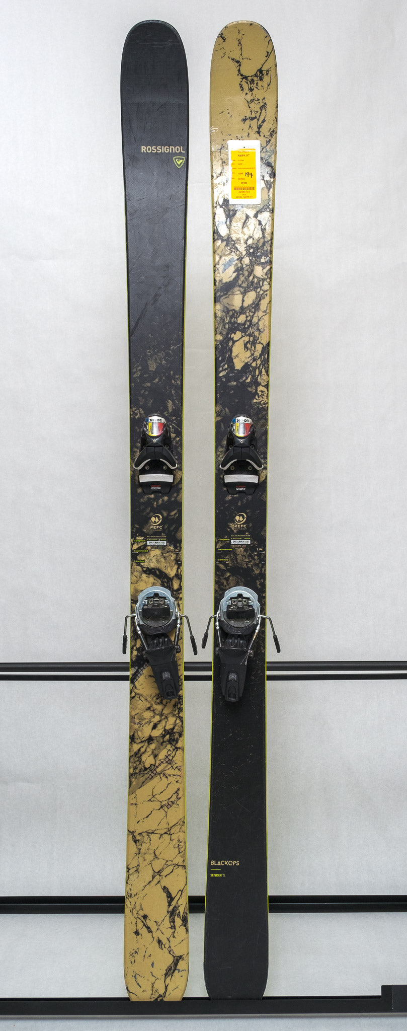 USED - Rossignol Black Ops Sender Ti with Pivot 14 Bindings - A black ski with a yellow and white logo on top, featuring a marbled pattern of tan and black.