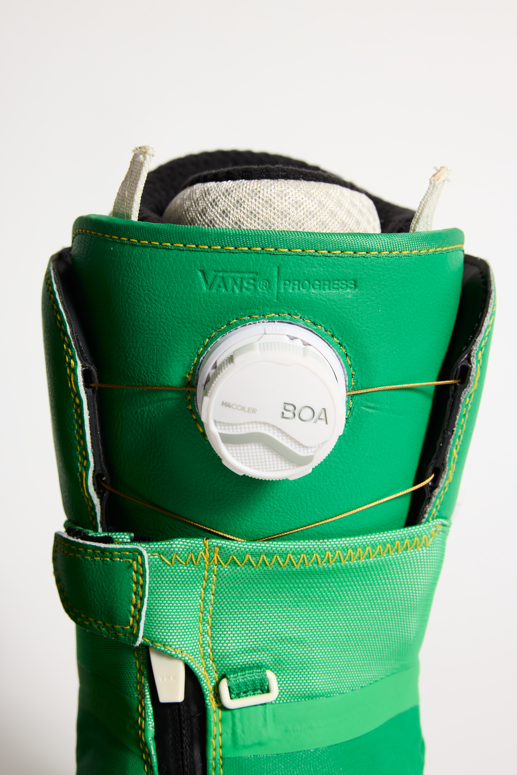 Vans snowboard boot close-up: BOA dial on green cuff with yellow stitched strap detail