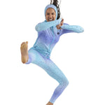 Airblaster Women's Classic Ninja Suit 2025 - A woman with long brown hair wearing a light blue and purple gradient ninja suit, featuring black speckles, posing in a dynamic kick pose.