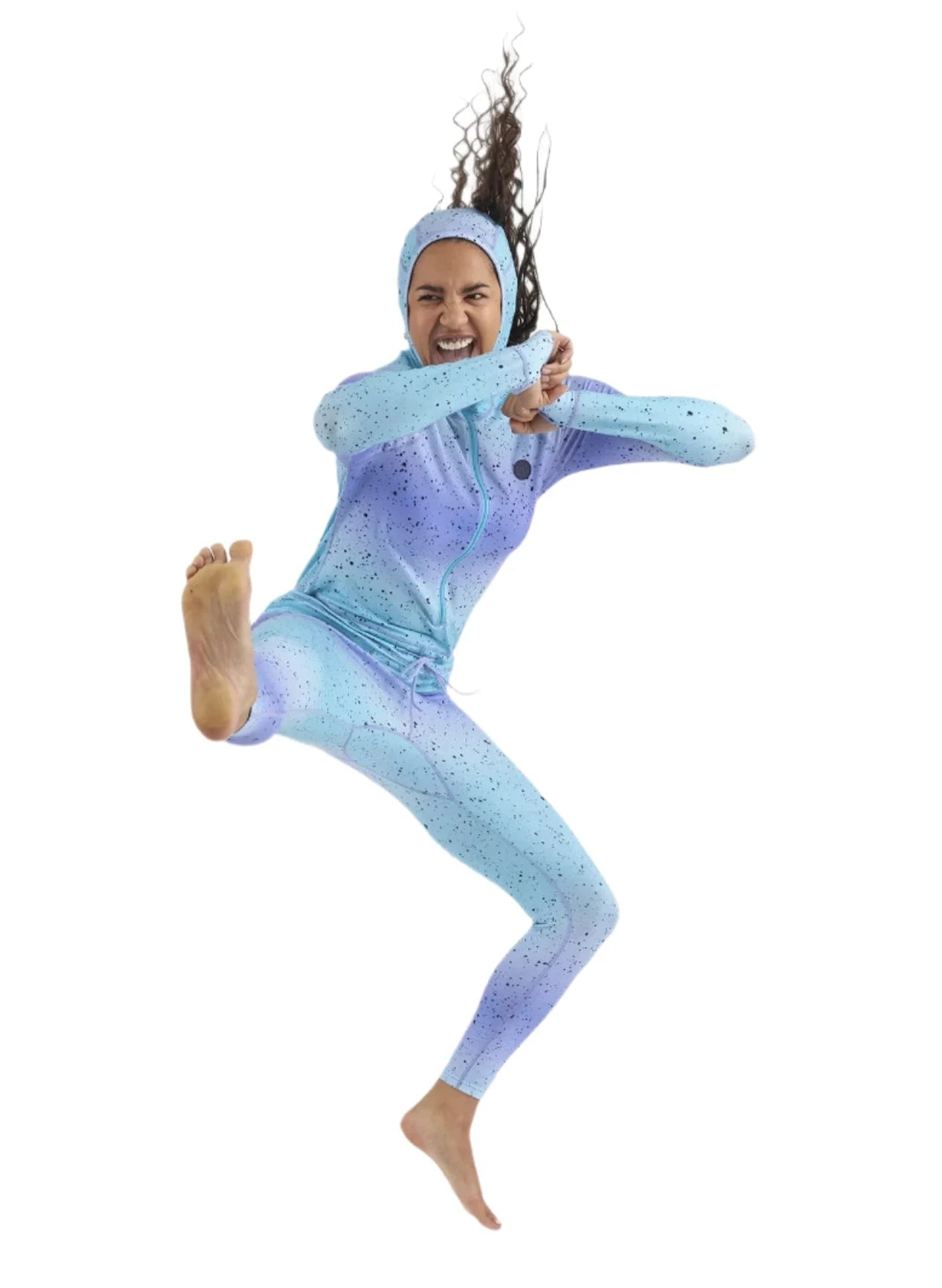 Airblaster Women's Classic Ninja Suit 2025 - A woman with long brown hair wearing a light blue and purple gradient ninja suit, featuring black speckles, posing in a dynamic kick pose.
