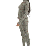 Airblaster Women's Hoodless Ninja Suit 2025 - A woman with long dark braids wears a sage green ninja suit adorned with small, repeating images of various snowboard boots and bindings in red, white, black, and brown.