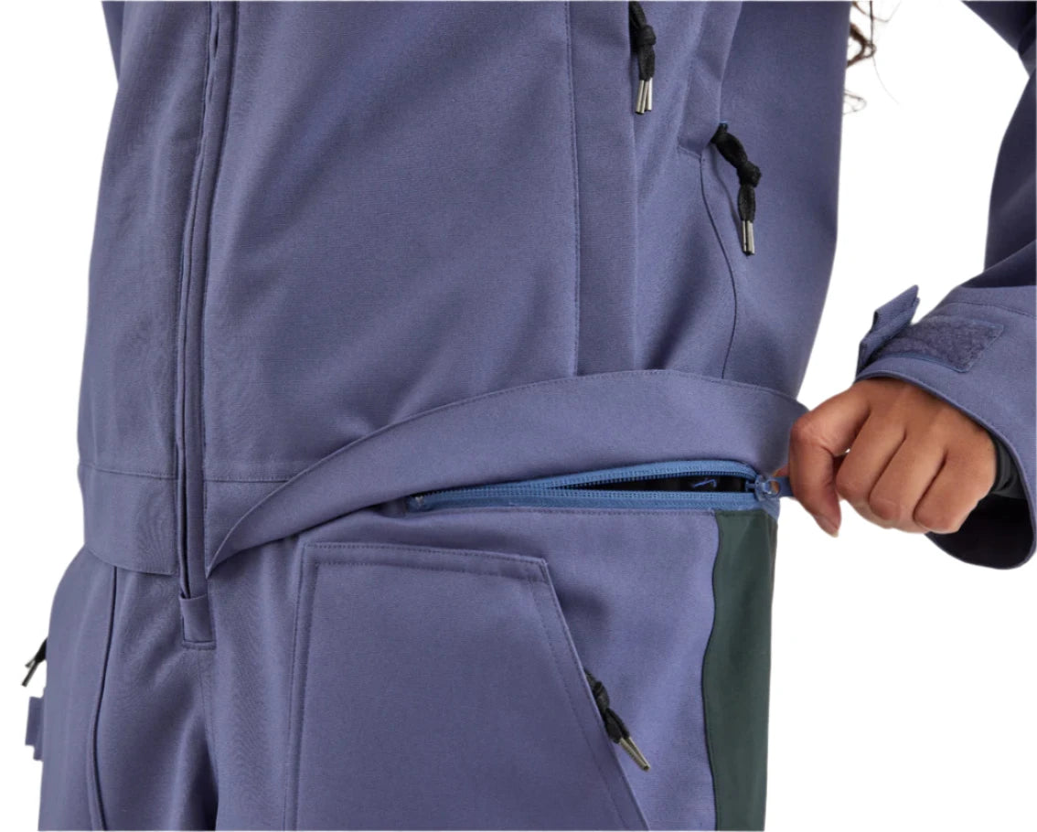 Airblaster Women's Stretch Freedom Suit 2025 - A woman wearing a purple snowsuit with black zippers and silver tips, standing in front of a white background.