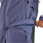 Airblaster Women's Stretch Freedom Suit 2025 - A woman wearing a purple snowsuit with black zippers and silver tips, standing in front of a white background.