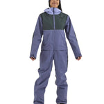 Airblaster Women's Stretch Freedom Suit 2025 - A woman wearing a blue and black snowsuit with a hood, standing in front of a white background.