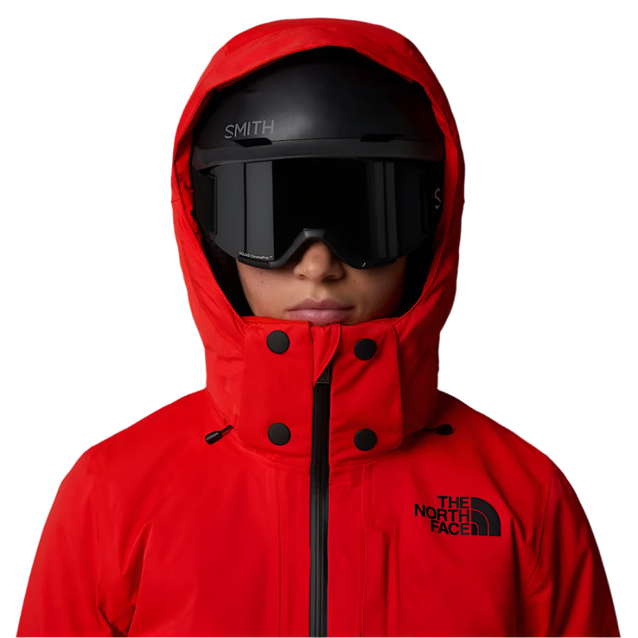 North Face Women's Lenado Insulated Jacket - A woman wearing a red ski jacket with black buttons and a hood, standing in front of a white background.