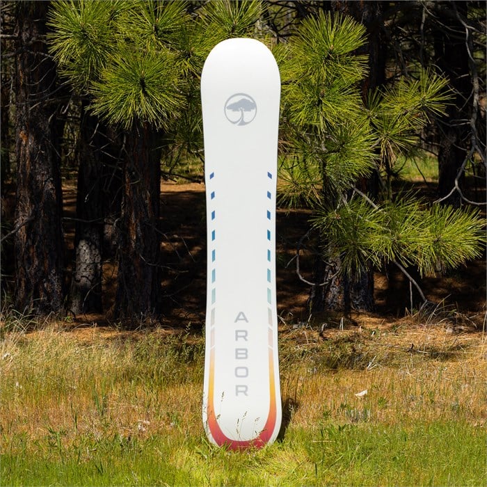 Arbor Women's Mantra Rocker Snowboard 2024 - A white snowboard with a circular logo featuring an image of a tree in the top center, and the word "ARBOR" printed vertically along the bottom edge.